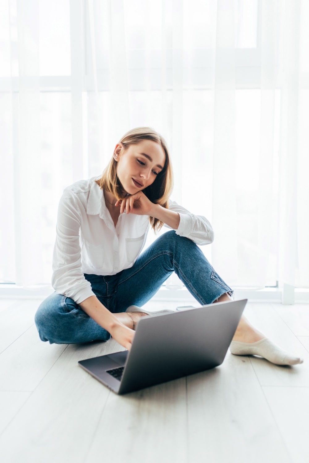 attractive-young-woman-surfing-her-laptop-sitting-floor-min